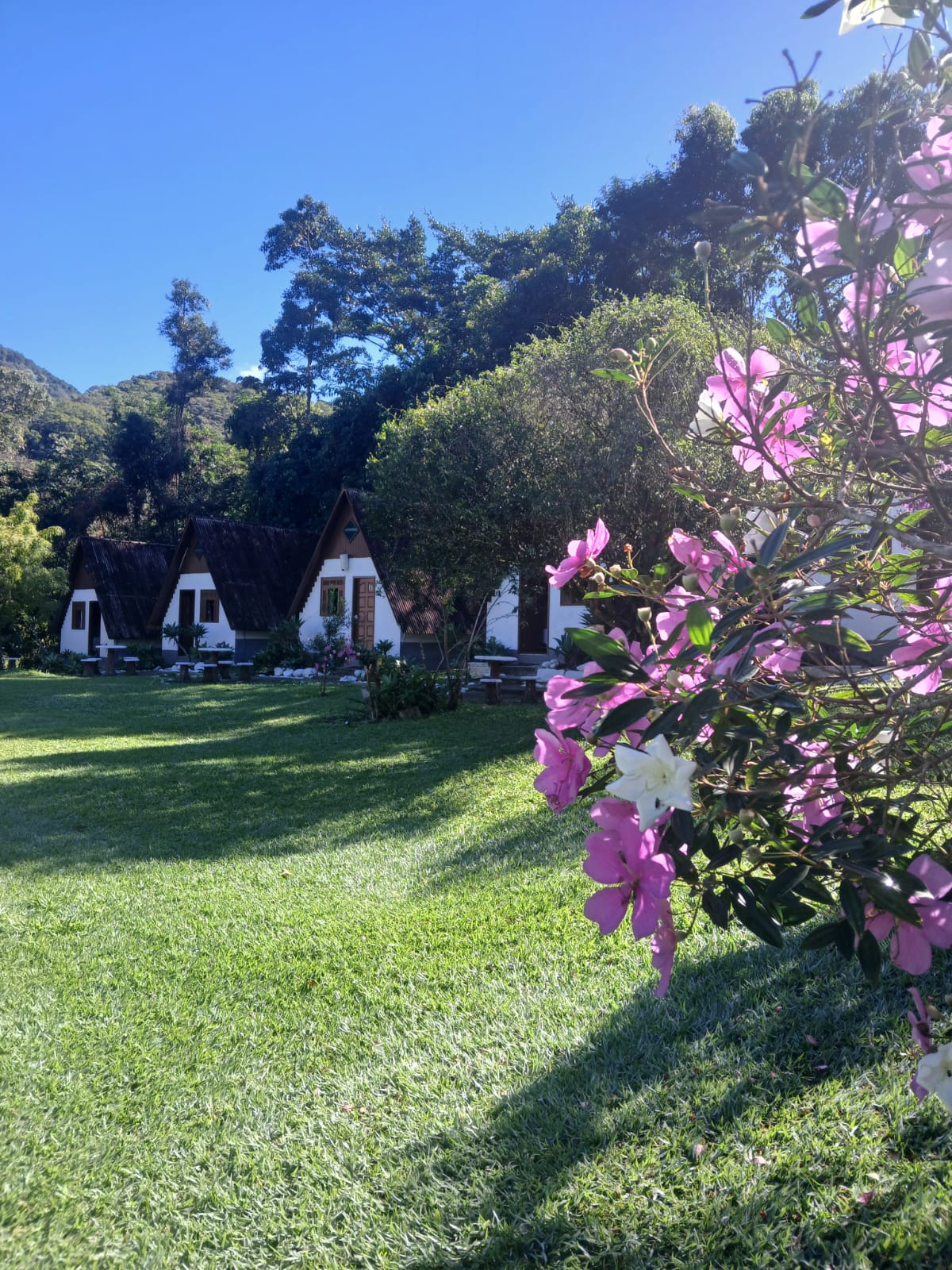 Chalés brancos da Pousada Riacho Doce com jardim florido e montanha ao fundo